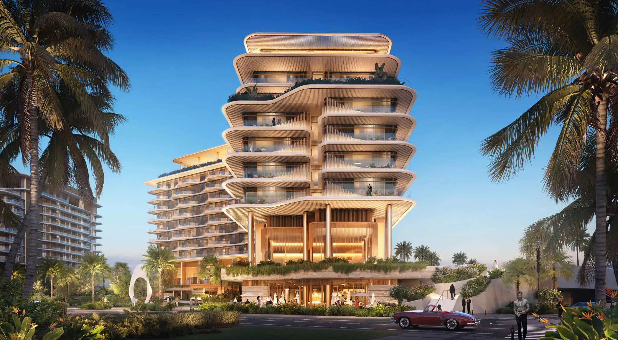 Modern multi-story building with layered, curved balconies surrounded by palm trees, landscaped gardens, and people walking near a parked red convertible car at dusk.
