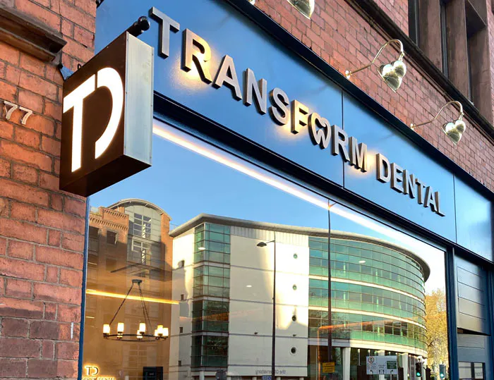 Transform Dental sign in metallic letters on a glass storefront reflecting nearby buildings and streetlights.