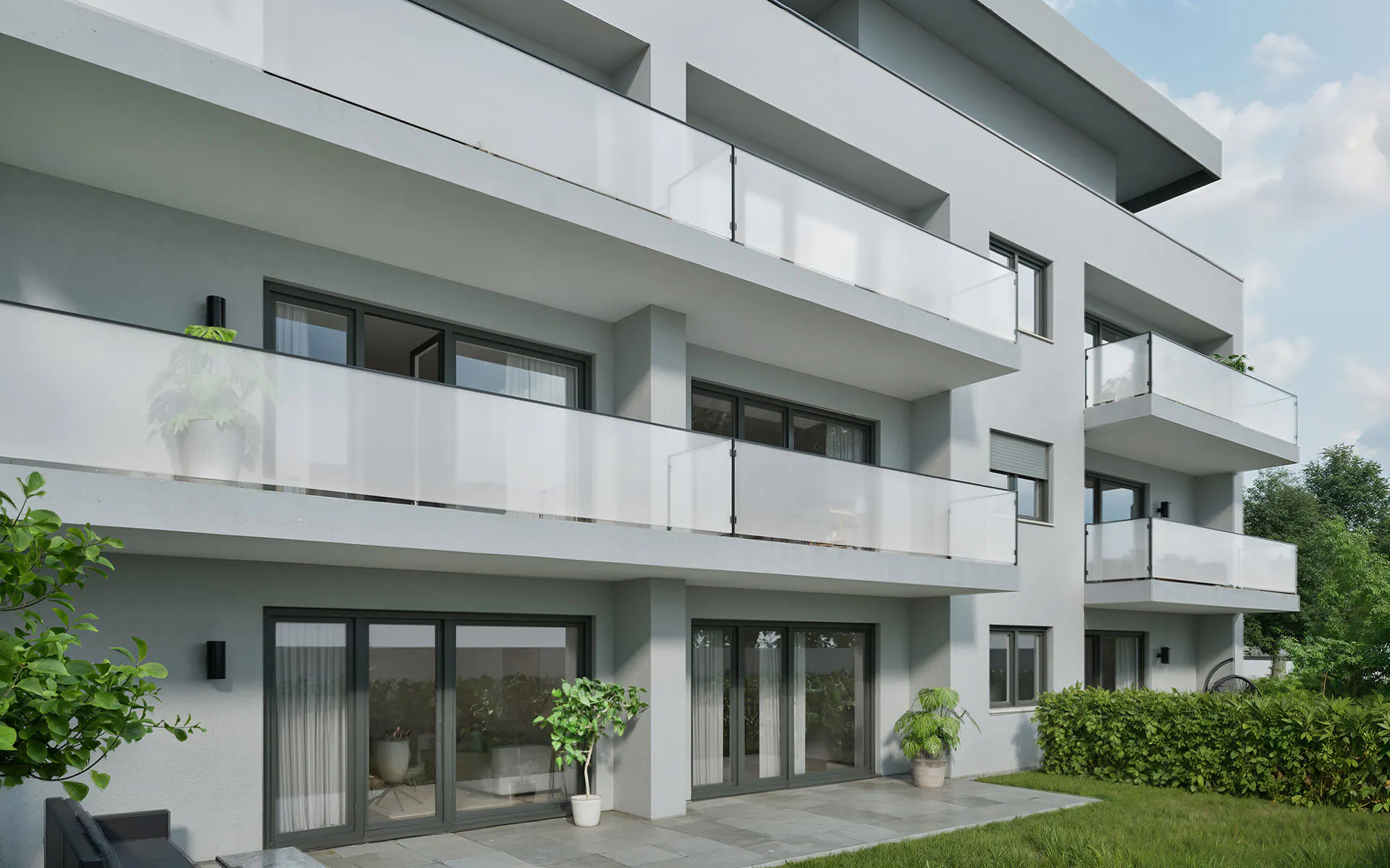 Mehrstöckiges modernes Wohngebäude mit Balkonen, Glasgeländern, großen Fenstern und einigen Pflanzen auf einer gepflasterten Terrasse und im Gartenbereich.