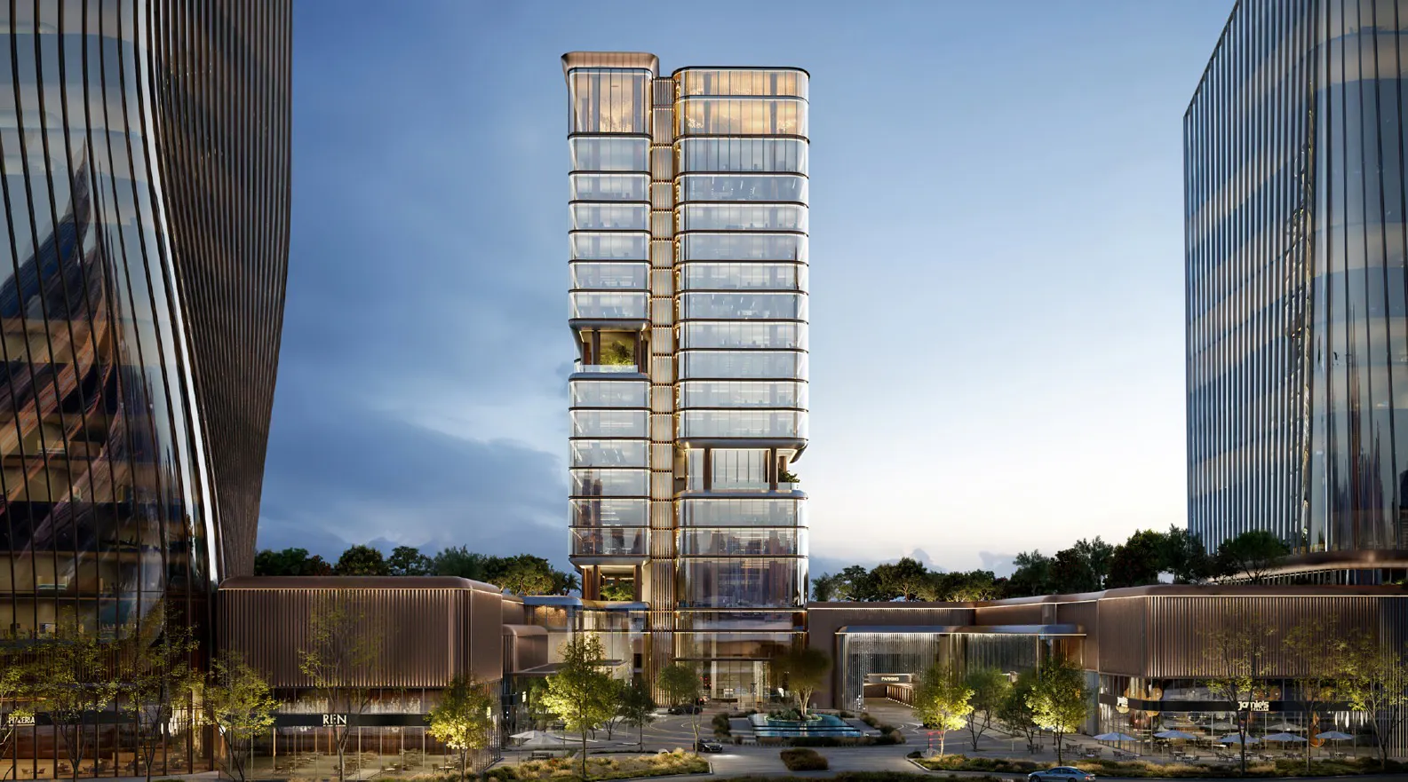 Tall modern glass building with rounded corners and illuminated horizontal lines, flanked by two similar high-rise structures, with trees and a water feature in the foreground at dusk.