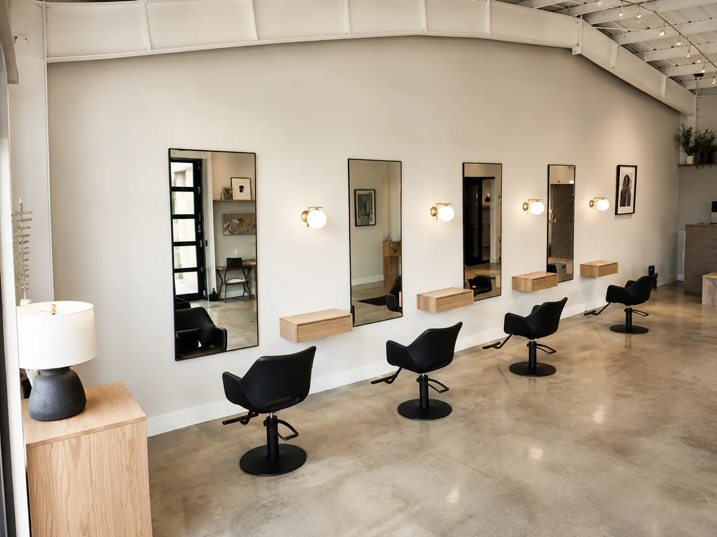 row of black salon chairs in front of mirrors in a minimalist hair salon