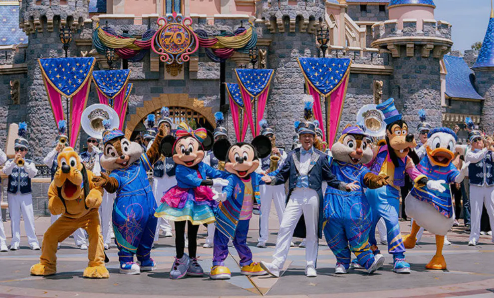 Mickey Mouse, Minnie Mouse, Donald Duck, Goofy, Pluto, Chip, and Dale with a performer in front of a decorated castle, surrounded by a marching band.