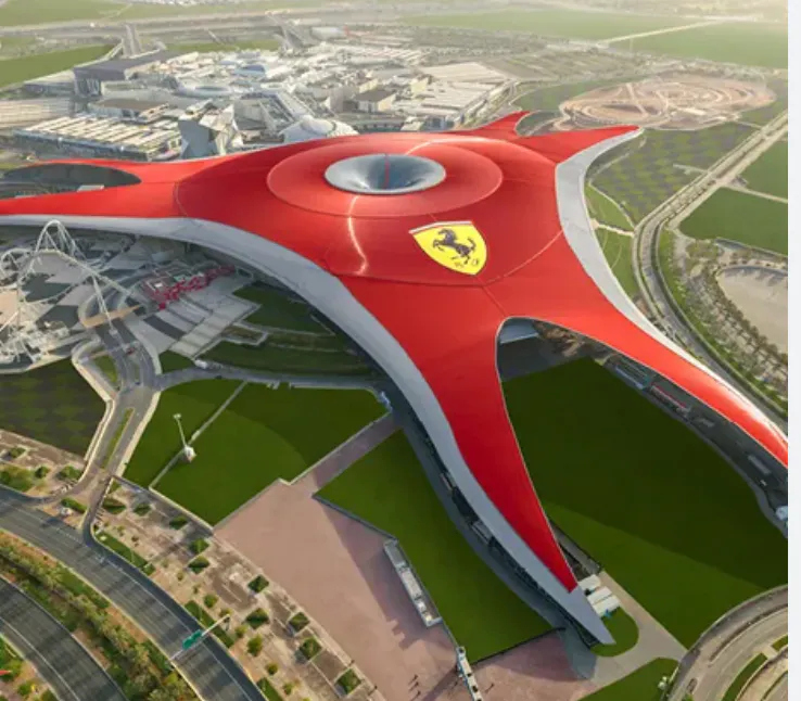 Large red building with a central circular opening and Ferrari logo on top, surrounded by roads and green spaces, resembling a star or three-pronged structure.