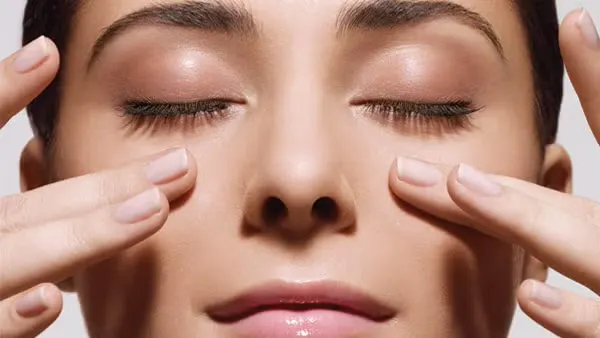 Close-up of a woman with closed eyes gently massaging her face with her fingertips