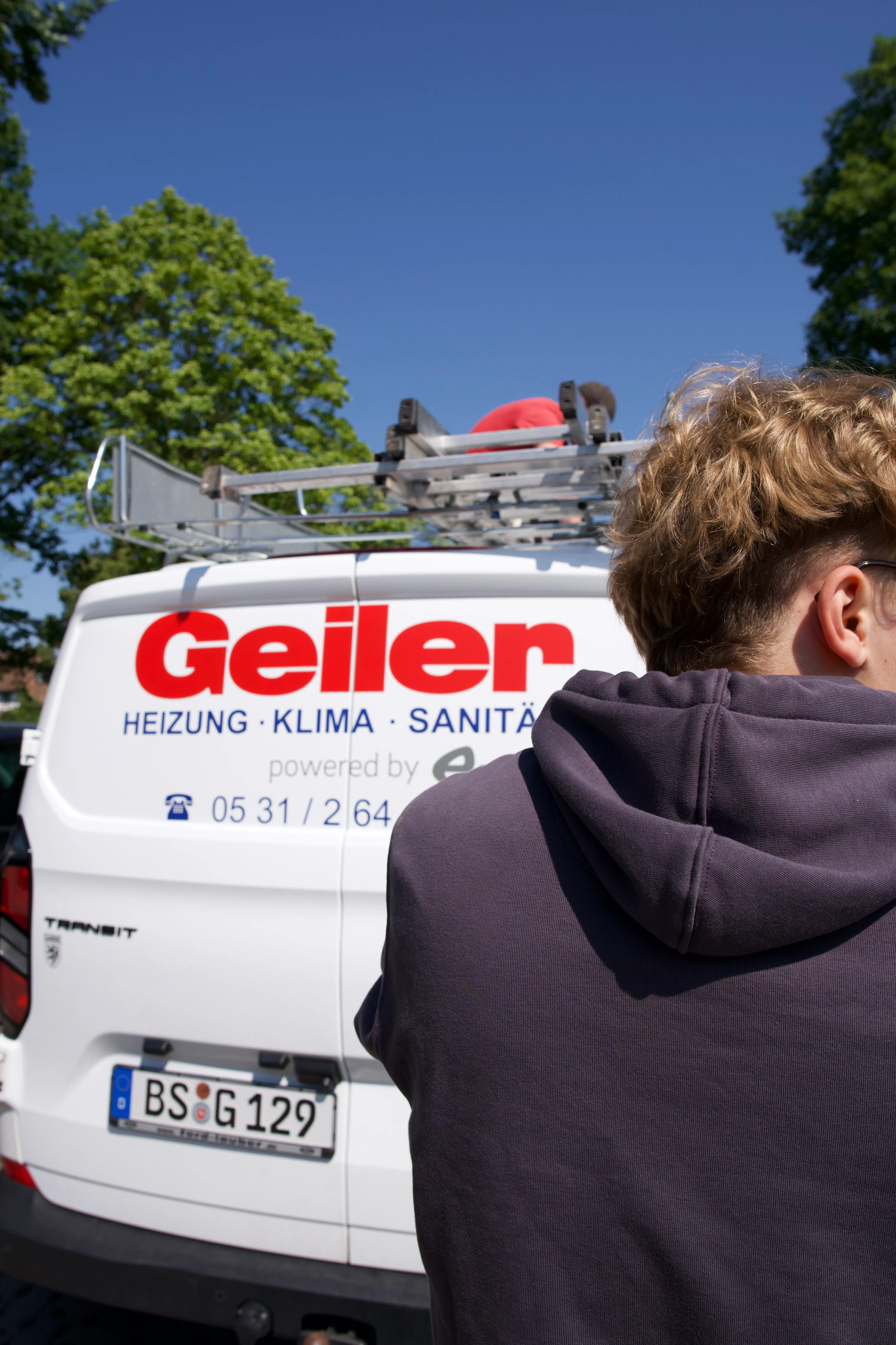 Van with the company name "Geiler" and services in heating, climate control, and sanitation, parked outdoors with a person in a dark hoodie in the foreground.