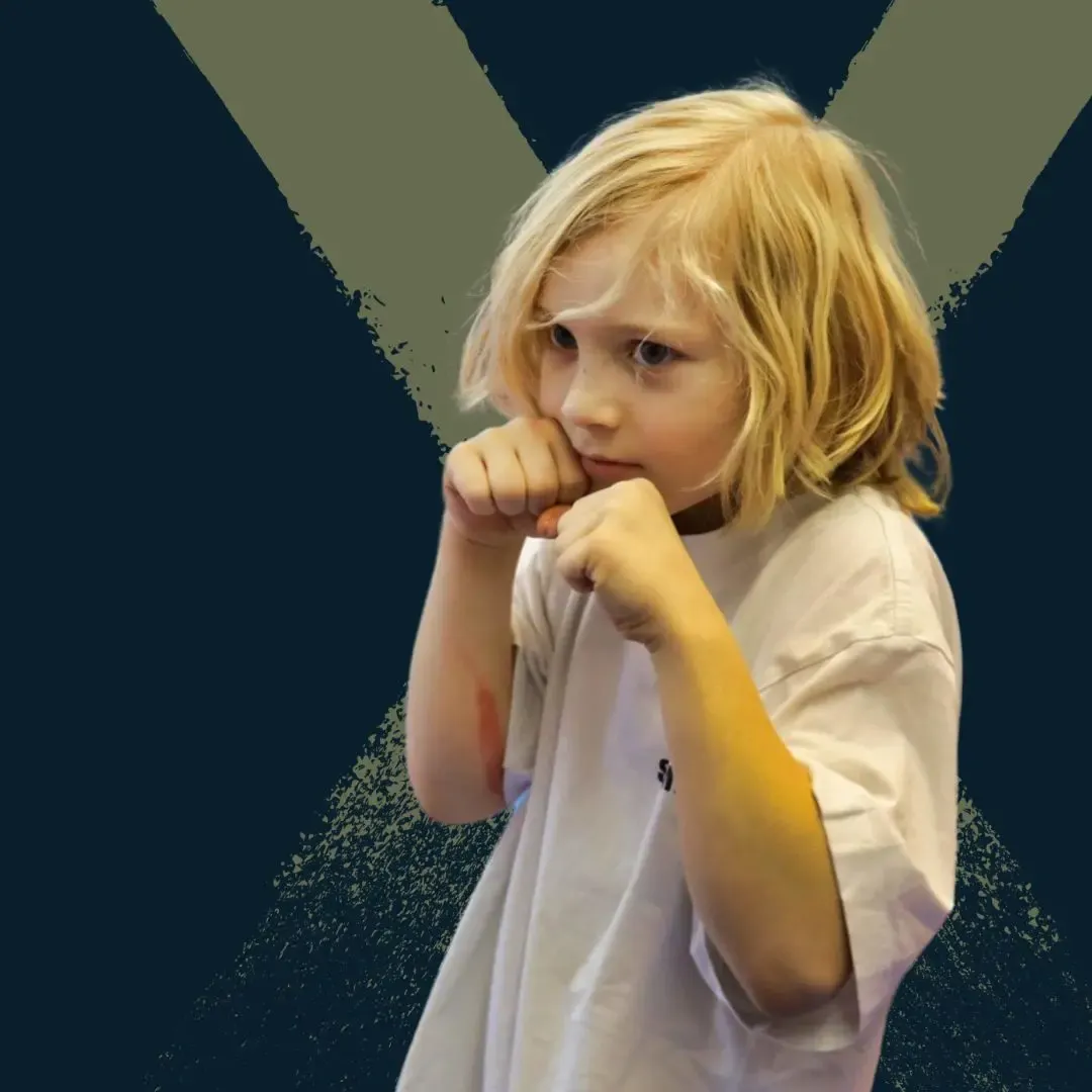 Blondes Kind in weißem T-Shirt hält die Fäuste vor das Gesicht in einer kämpferischen Haltung vor dunklem Hintergrund mit großem, undeutlichem X.