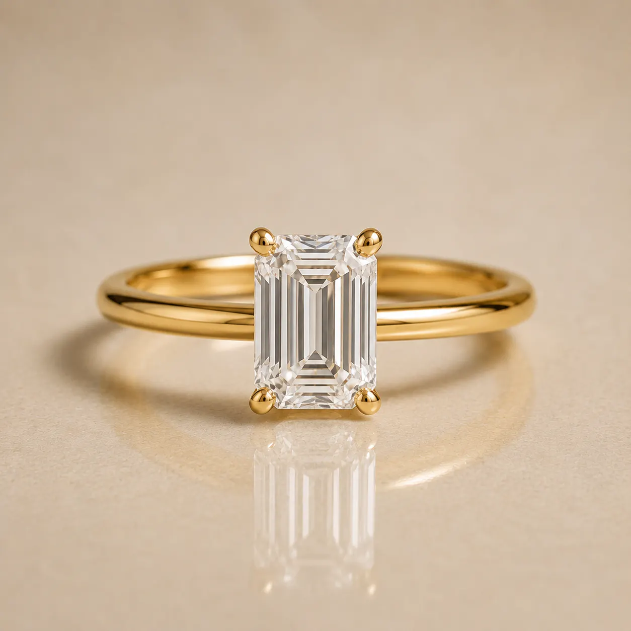 Gold ring with a large rectangular emerald-cut diamond held by four prongs, displayed on a beige surface with the ring's reflection visible.
