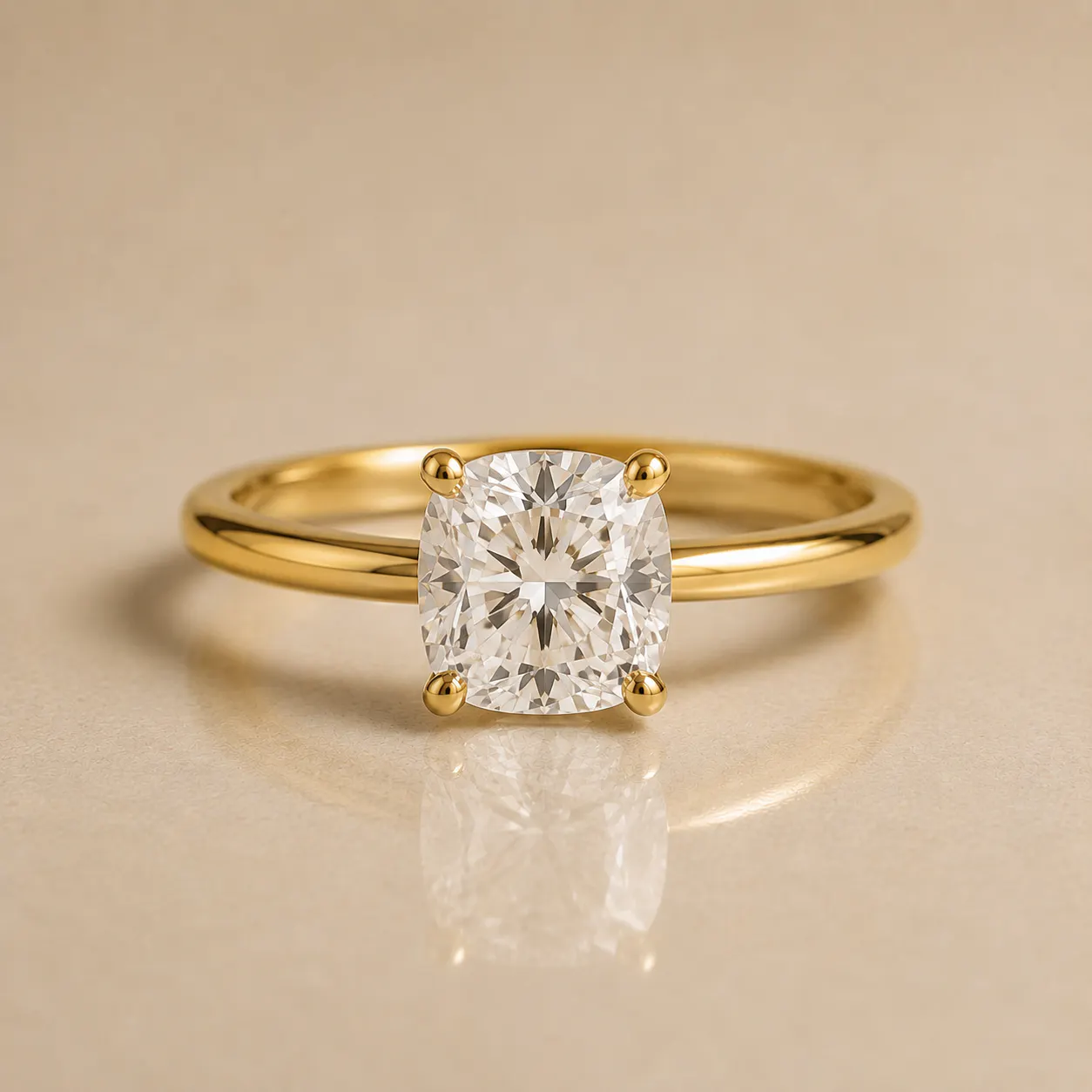Gold ring with a cushion-cut diamond held by four prongs on a polished band, resting on a smooth beige surface.