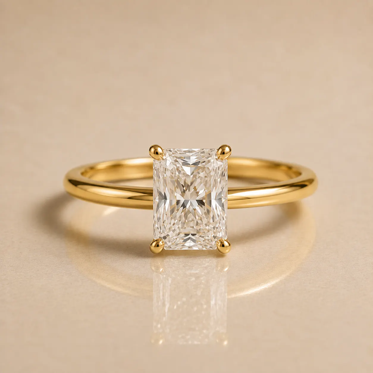 Gold ring with a rectangular radiant-cut diamond solitaire set on a simple, polished gold band, displayed on a beige surface.