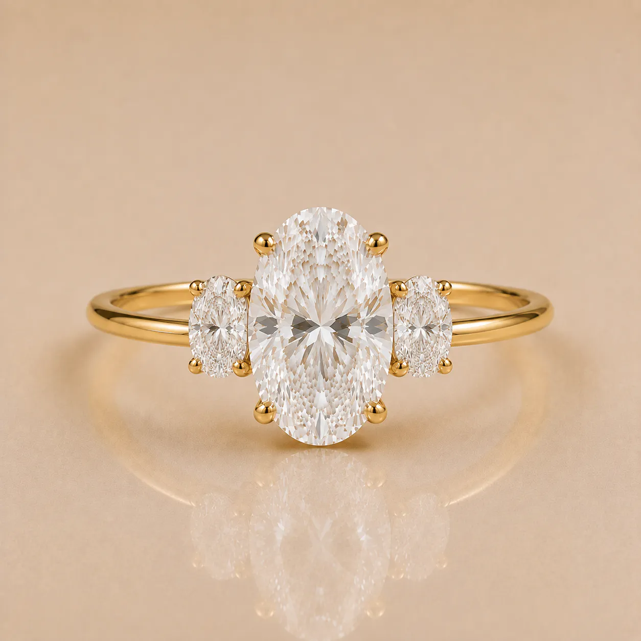 Gold ring with three oval-cut diamonds, a large central diamond flanked by two smaller diamonds on each side, set on a thin gold band against a beige background.