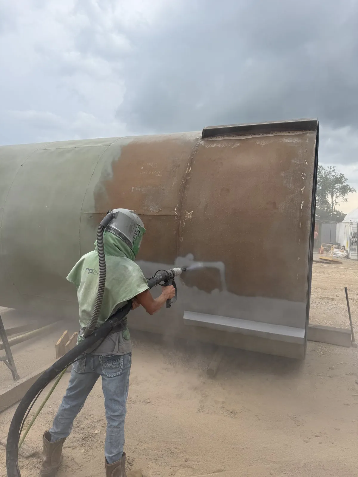 worker sandblasting a rusted tank