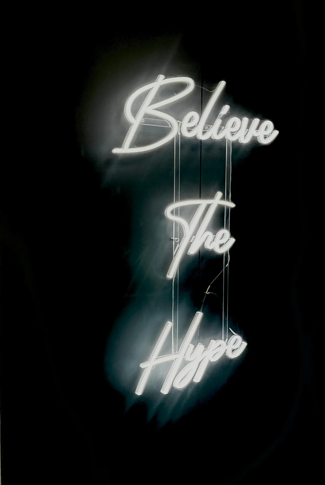 White neon sign reading Believe The Hype on a black wall