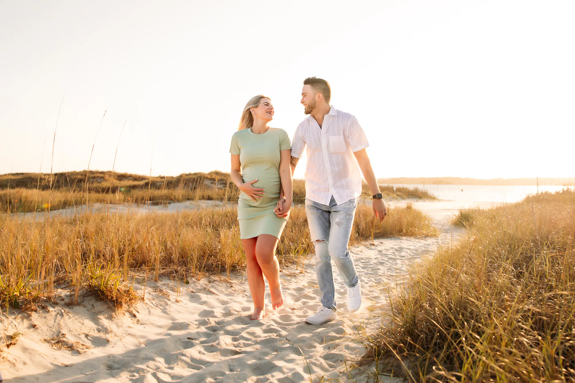 Expecting couple walking through the dunes at sunset