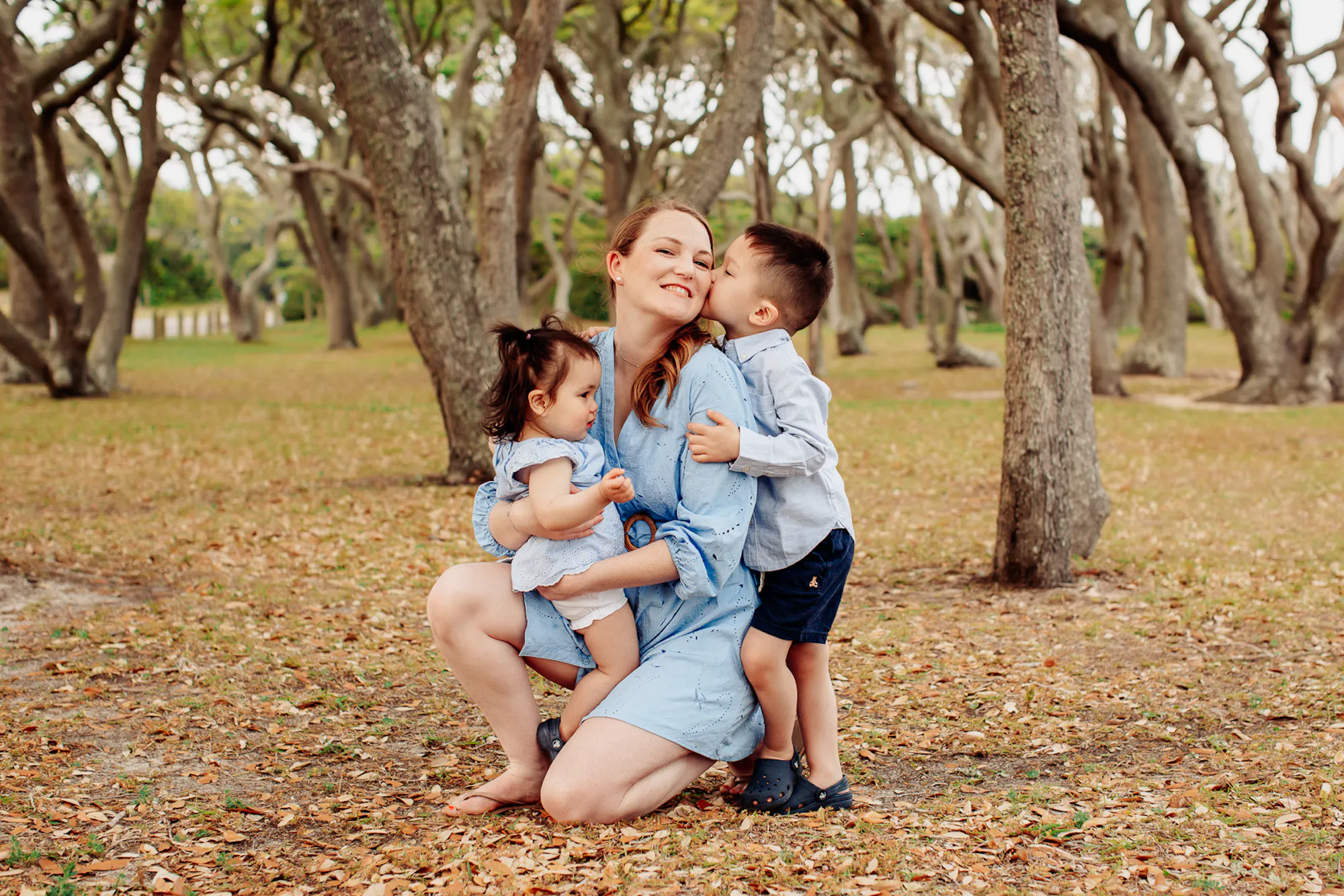Mother kneeling with her two children under oak trees