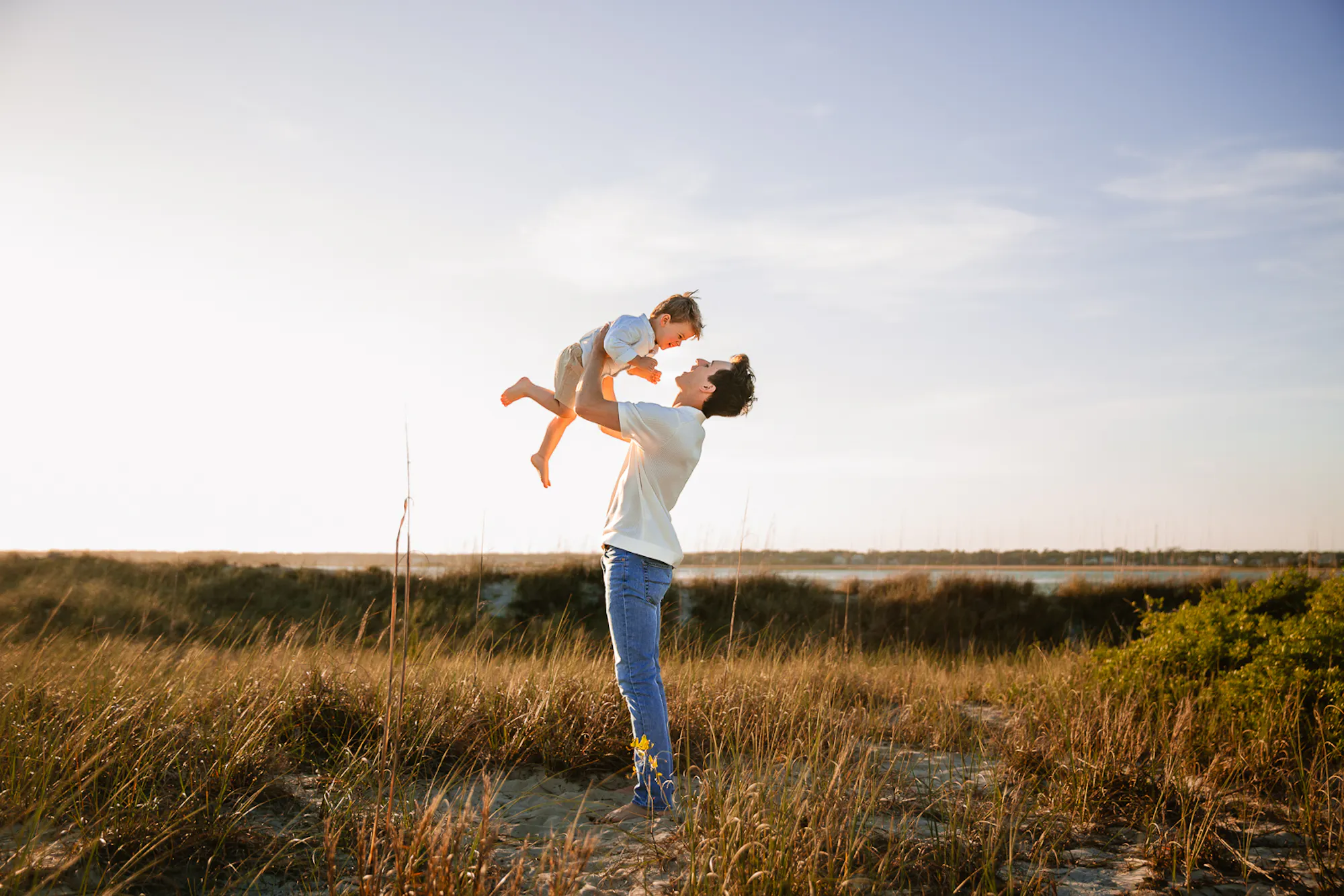 Father lifting his child in the dune grass at sunset