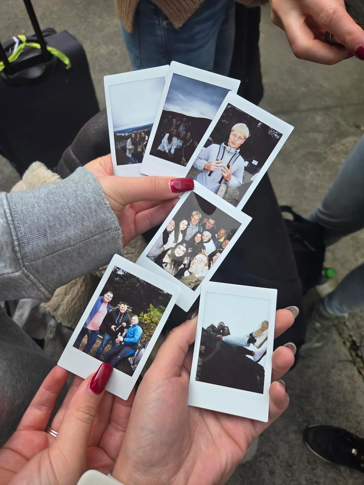 Hands holding six instant photos showing groups of people posing outdoors and a portrait of a young person in a jacket.