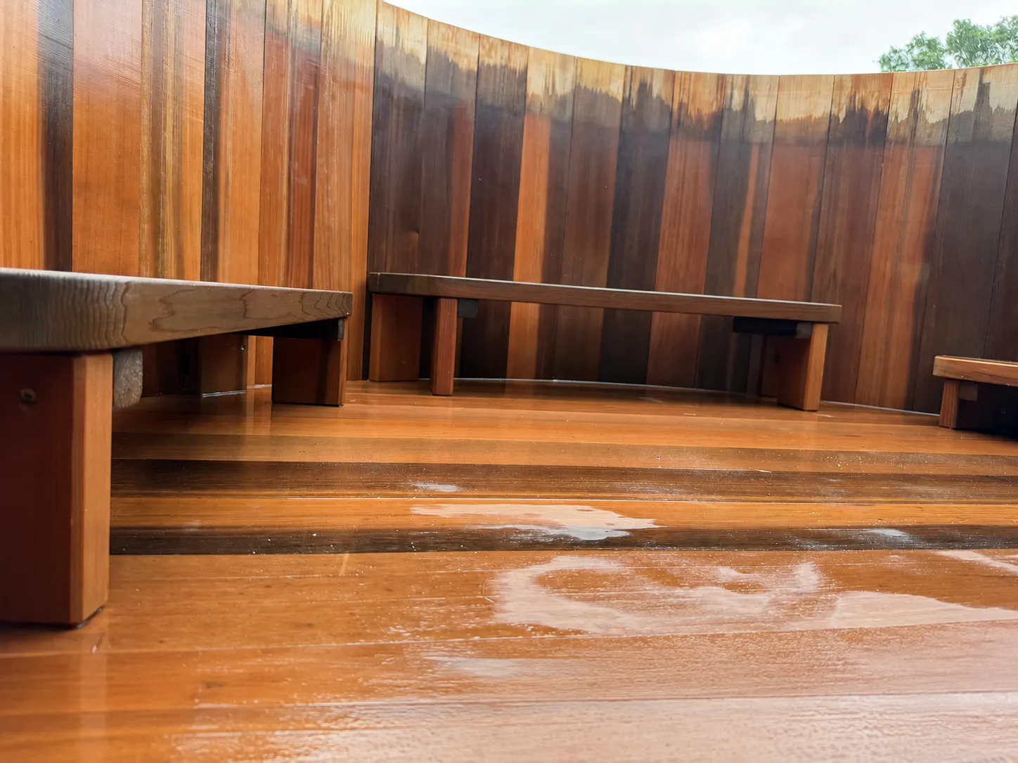 Curved wooden seating area with three bench-style seats and a wet wooden floor reflecting light.