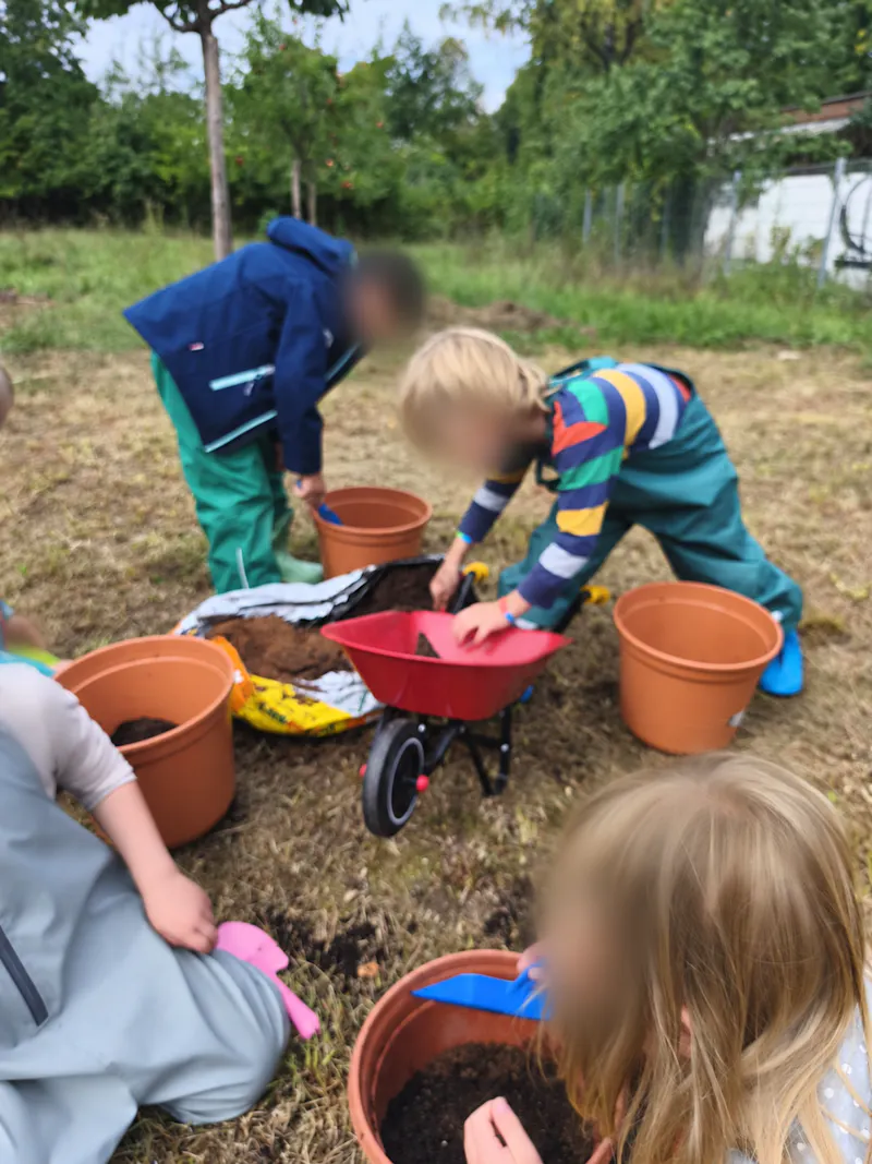 Kinder mit Erde, Pflanztöpfen und kleiner Schubkarre