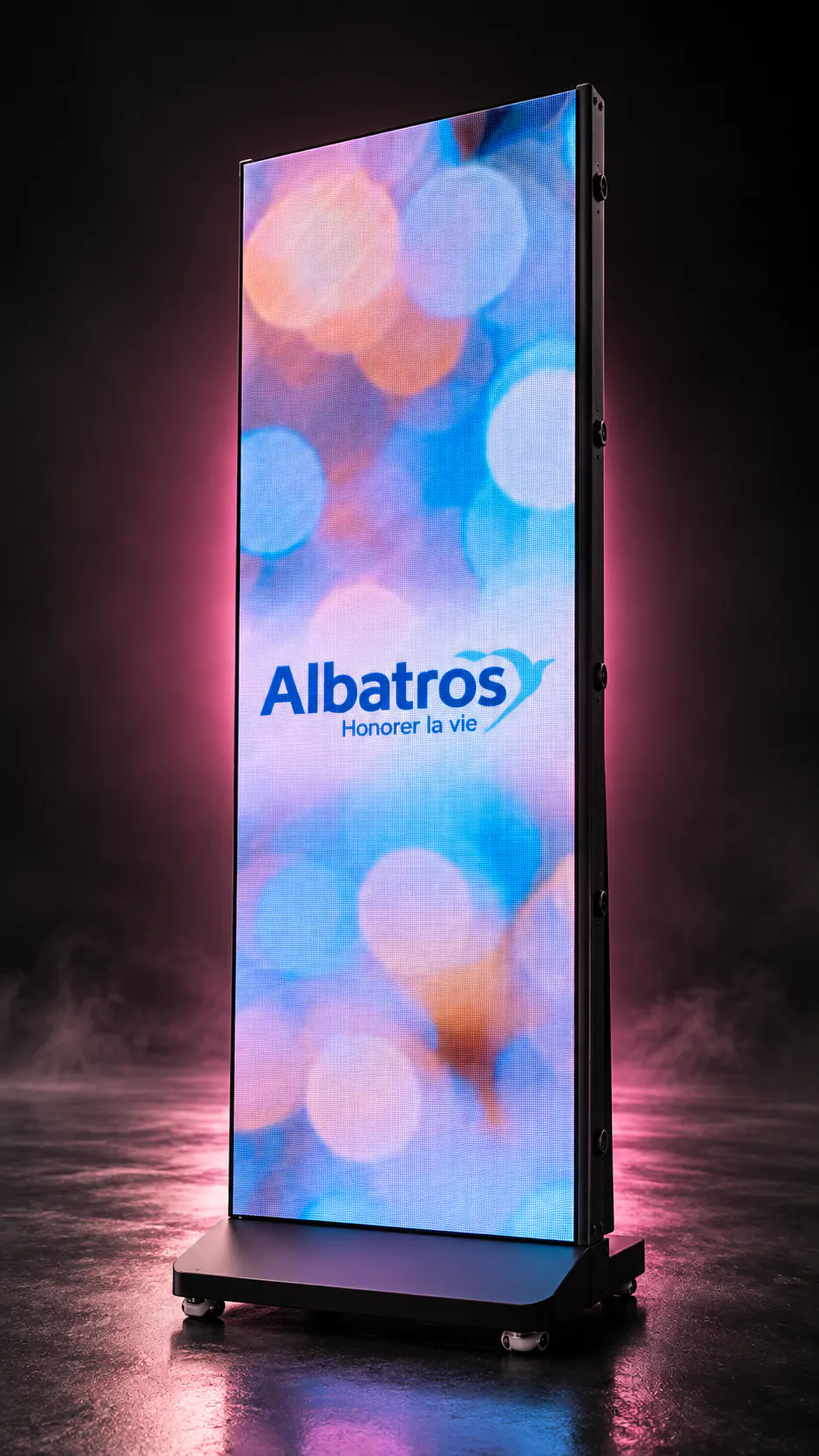 Tall digital display screen on wheels showing the logo "Albatros" with the tagline "Honorer la vie" against a colorful blurred light background.