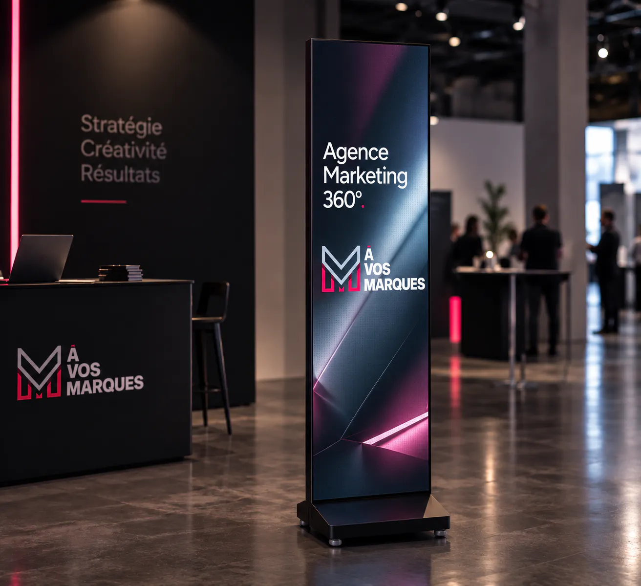 Digital display screen in a marketing agency lobby showing "Agence Marketing 360°" and "À Vos Marques" with a logo, beside a counter with a laptop and stack of brochures.