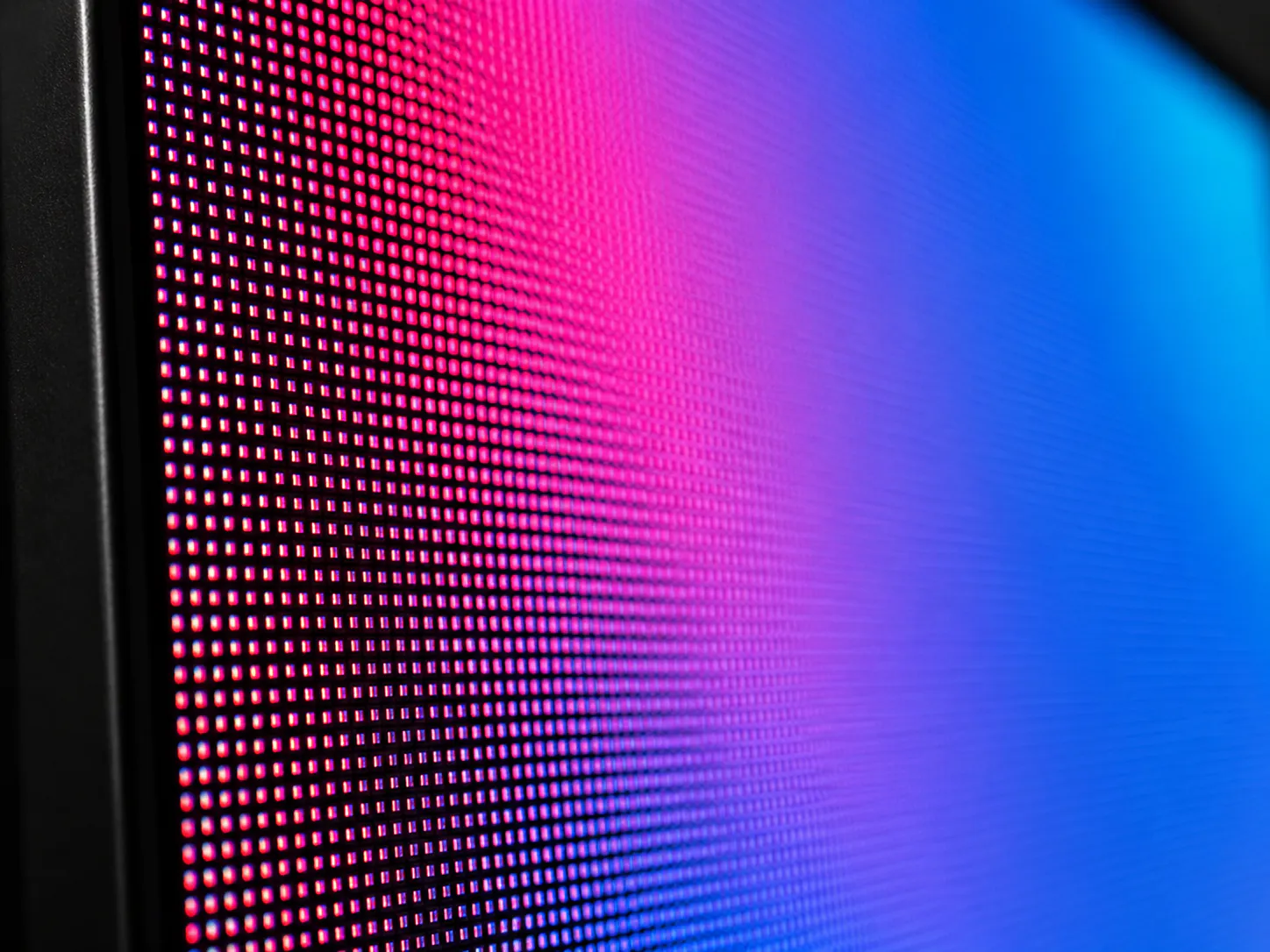 Close-up view of a digital screen showing individual red, blue, and purple pixels forming a gradient from pink to blue.
