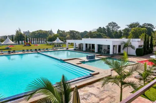 Outdoor rectangular swimming pool with clear blue water, surrounded by lounge chairs, a white pool house, palm trees, and a green lawn with tents in the background.