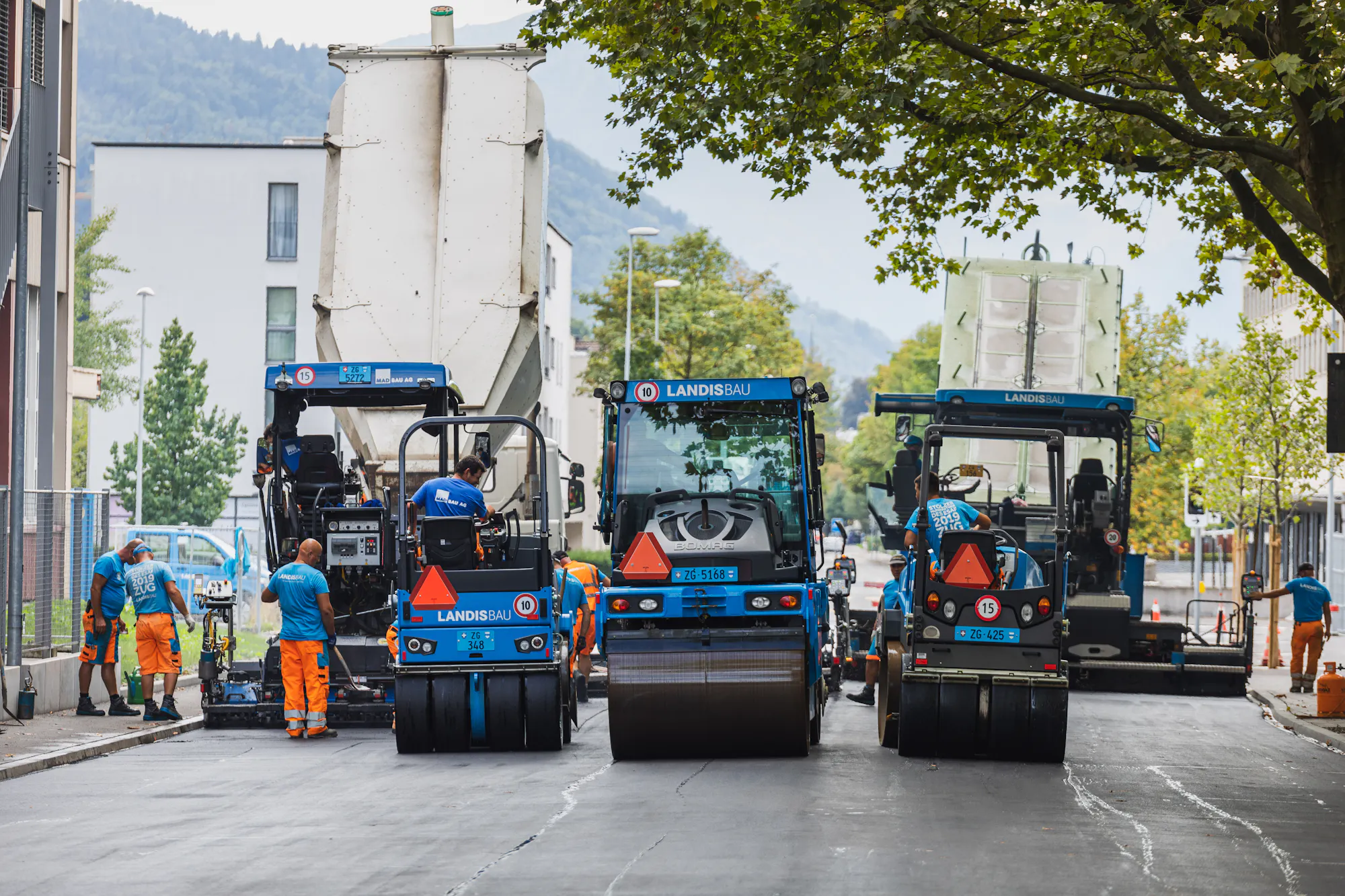 Blaue Walzen und Belagsfertiger von Landis Bau auf der Baustelle in Zug