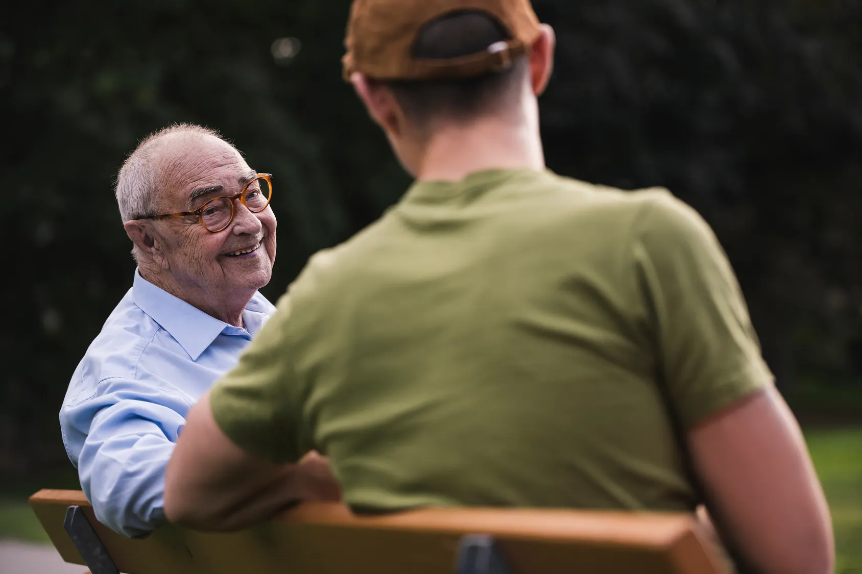 Smiling retiree talking with a younger man on a park bench