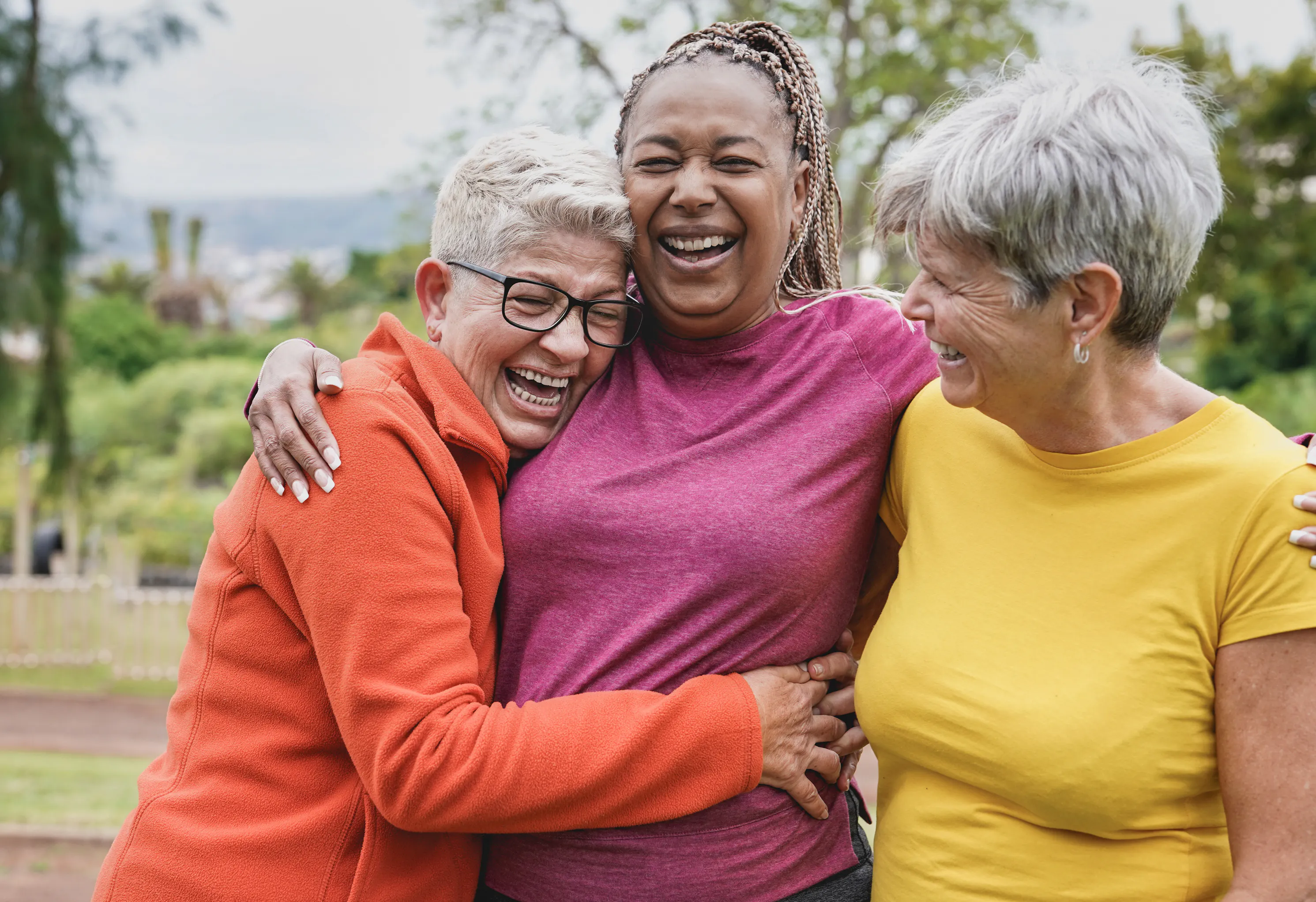 Three retired women laughing and hugging outdoors
