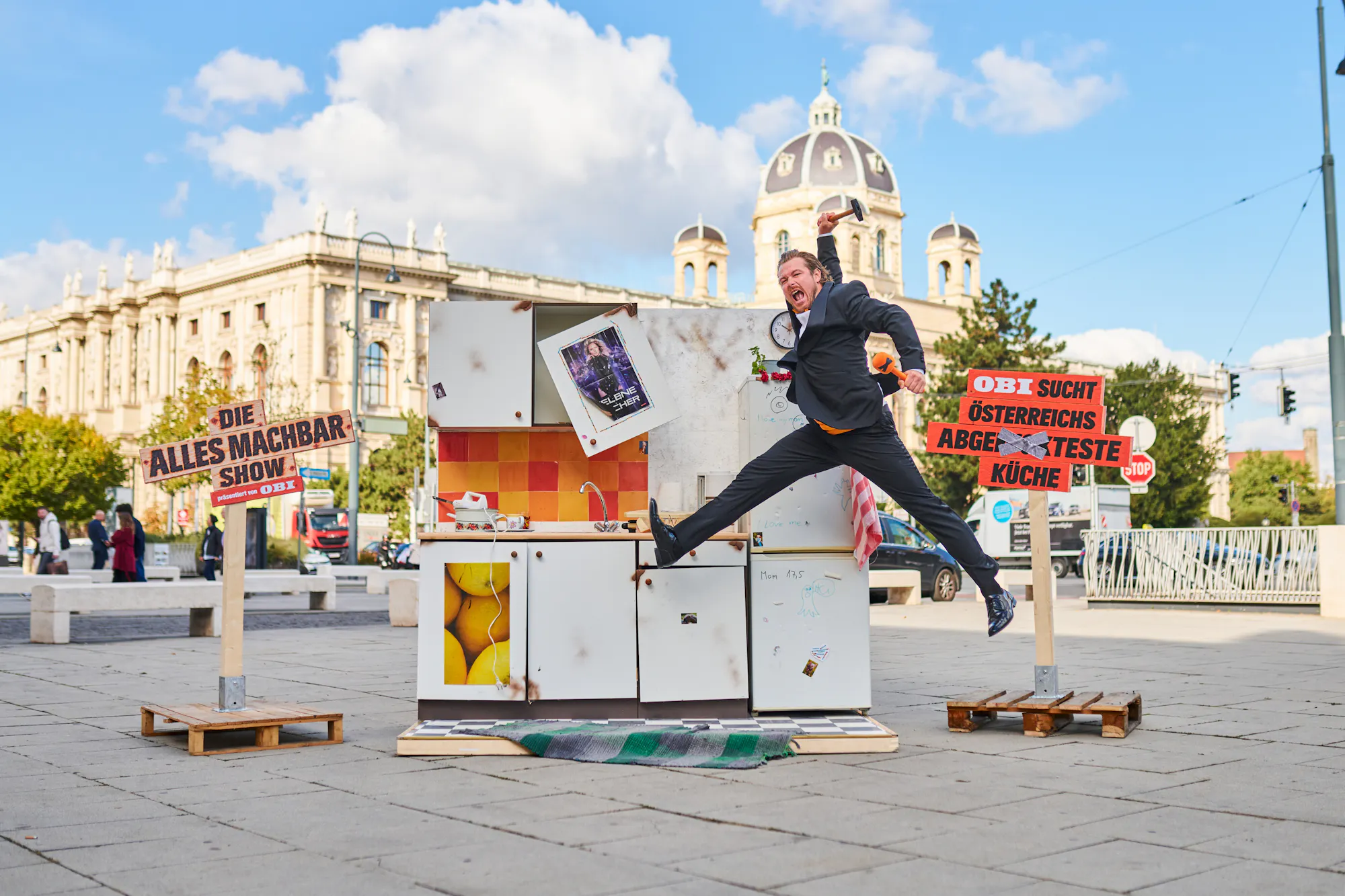 Moderator springt vor einer kaputten Küche mit Schildern der OBI Alles machbar Show in Wien