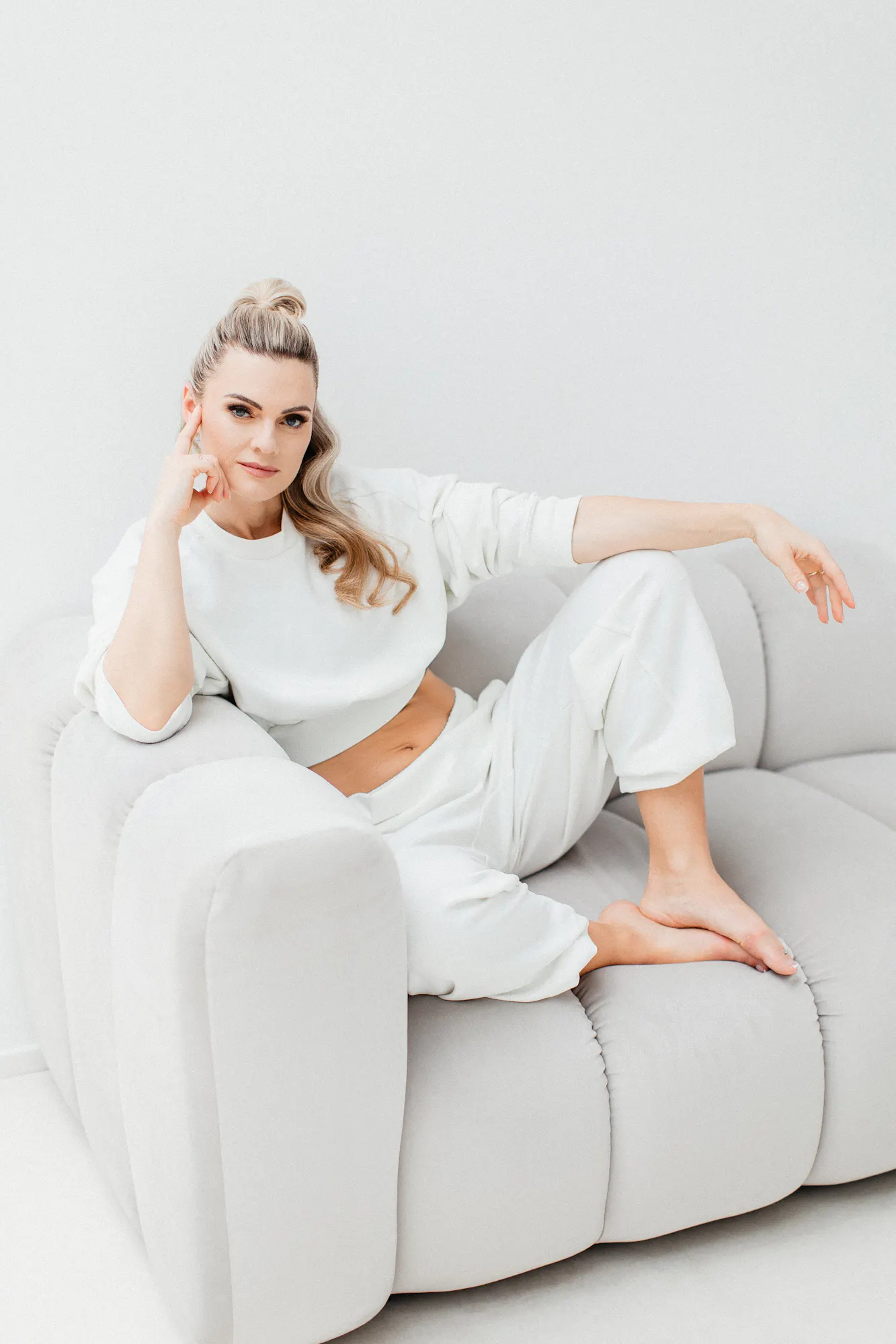 Marie MENtorin sitzt in Weiß auf einem hellen Sofa und blickt in die Kamera