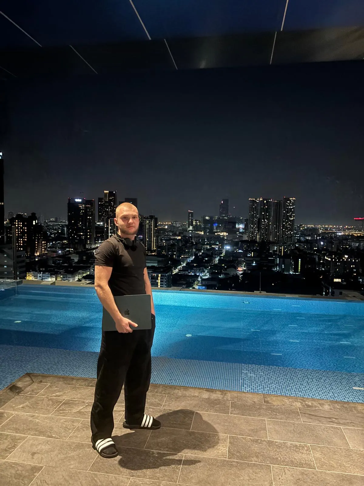 David Andreju on a rooftop at night with the illuminated city skyline behind him
