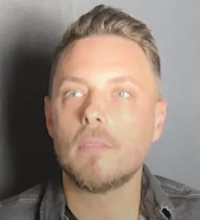 Man with short light brown hair, light beard, and blue eyes looking slightly upward, wearing a dark collared shirt against a plain gray background.
